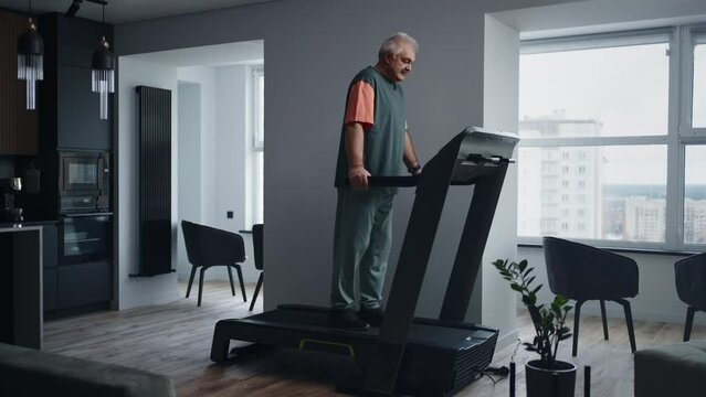 Mature Man Training At Home, Walking On Treadmill In Living Room, Healthy Lifestyle Of Old People