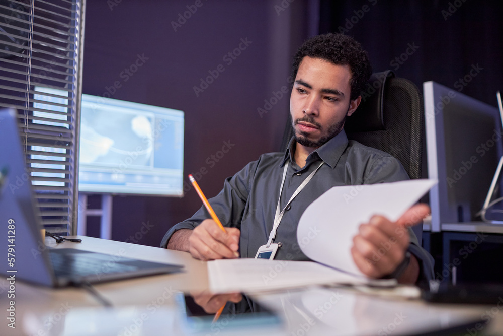 Poster portrait of male data scientist working with documentation at workplace in high tech office
