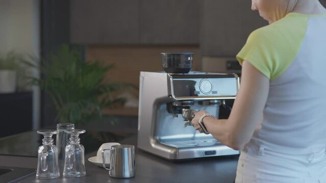 Caucasian female starts espresso machine and takes portafilter.