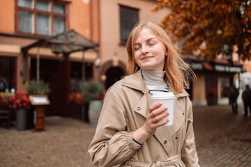 Portrait of happy nice woman drinks coffee while traveling in European old town enjoying cup of tea, coffee. Gdansk, Poland