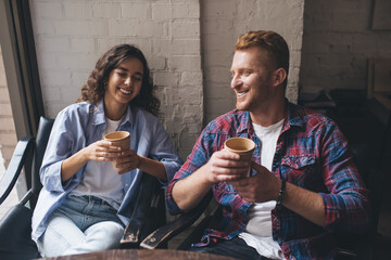 Cheerful Caucasian couple in love enjoying live communication and flirting bonding during cafeteria date indoors, carefree male and female with coffee smiling while talking about youth lifestyle