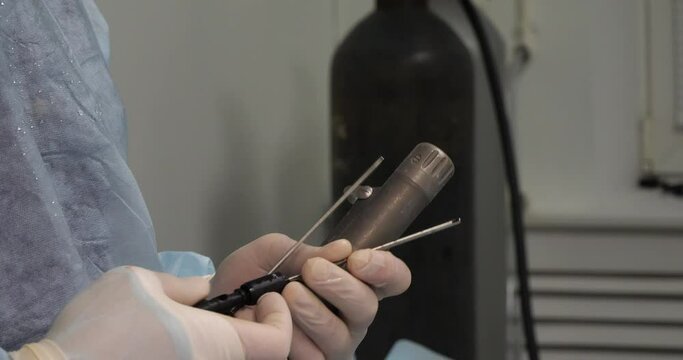 A veterinary surgeon prepares equipment for knee arthroscopy in a pet. The assistant's hands check the serviceability of the arthroscopic equipment before starting the operation on the pet's knee.
