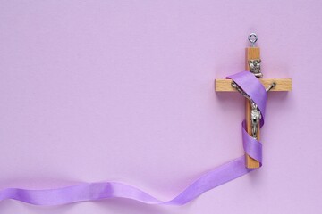 Christian religious wooden cross crucifix with violet ribbon on purple background. Catholic...