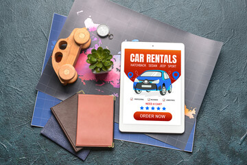 Obraz premium Tablet computer with open page of car rental website, maps and passports on dark background