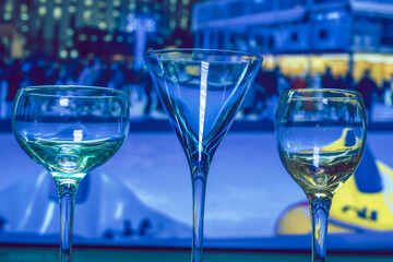 Two empty wine glasses and an empty cocktail glass in front of a blue background, nighttime led lighting reflected on glasses, nobody