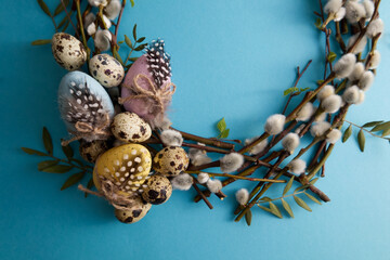 Spring willow wreath decorated with easter eggs and quail eggs on a blue background copy space