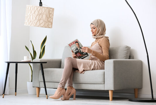 Beautiful Muslim woman reading magazine on sofa at home