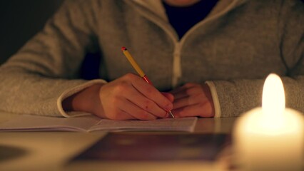 Hand of young man writing notebook by candlelight doing homework close up. Children doing school homework at home. Studying without electricity