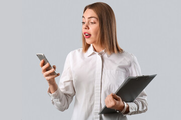 Fototapeta premium Female business consultant with clipboard using mobile phone on grey background