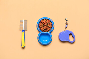 Bowl of dry pet food, grooming comb and leash on color background