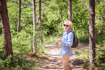 Senior woman hiking in forest trail. Recreation and healthy lifestyle outdoors, inspirational nature. Fitness and trekking and activity concept.