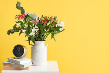 Vase with beautiful alstroemeria flowers, alarm clock and books on end table near yellow wall