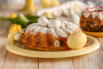 Plate with tasty Easter cake and painted eggs on white wooden table