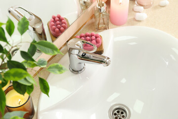 Table with white sink, burning candles and cosmetic products, closeup