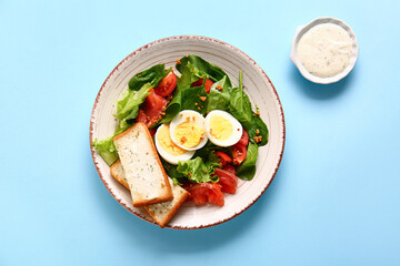 Plate of delicious salad with boiled eggs and salmon on blue background