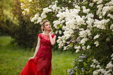 Beautiful woman in blooming lilac garden. Half-body Portrait in sunset light. Pretty young...