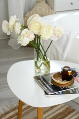 Vase with ranunculus flowers and magazines on table in bathroom, closeup