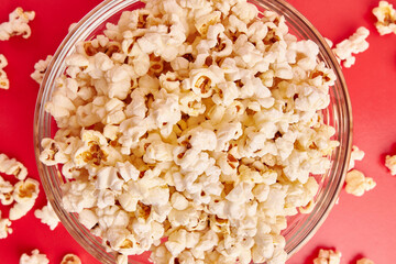 A bowl on a red background is completely filled with popcorn.