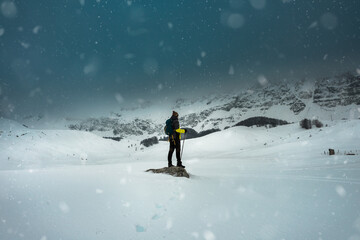 Hiker with backpack stand on rock in in heavy snowstorm. Winter on mountain Lebrsnik.