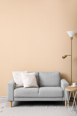 Grey sofa with cushions, lamp and table near beige wall
