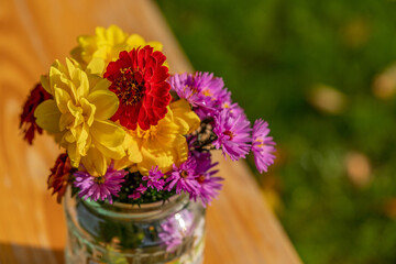 various colourful vibrant flower in glass jar on wooden table, flowers in vase in natural light