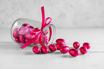 Overturned jar with chocolate Easter eggs on light wooden background
