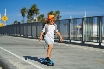 Kid boy riding skateboard in the road. Kid practicing skateboard. Children learn to ride skateboard in a park on sunny summer day. Boy on skateboard skating.