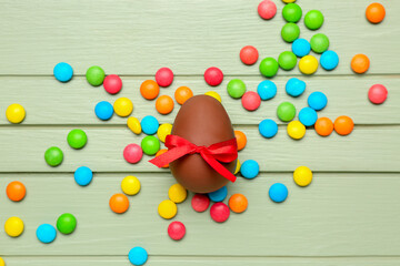 Candies and chocolate Easter egg tied with ribbon on green wooden background