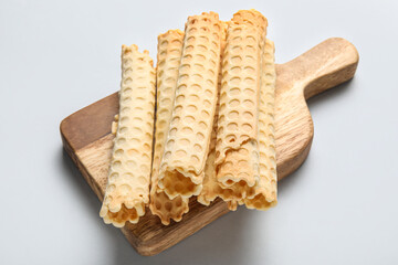 Board with delicious wafer rolls on grey background
