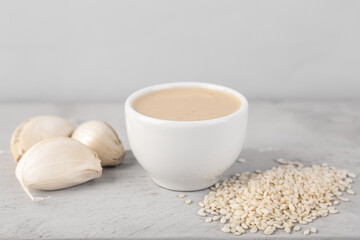 Bowl of tasty tahini, sesame seeds and garlic on table