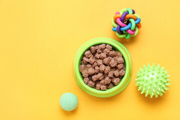 Bowl of wet pet food and balls on color background