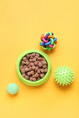 Bowl of wet pet food and balls on color background