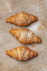Freshly baked croissants with sugar powder in a row over beige concrete background. Overhead view, close up