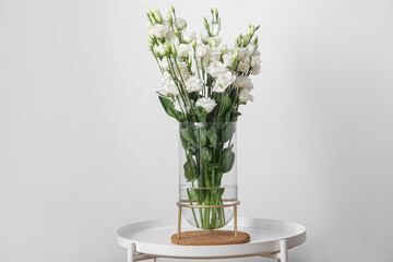 Vase with beautiful eustoma flowers on table near light wall