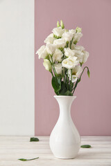 Vase with delicate eustoma flowers on table near color wall