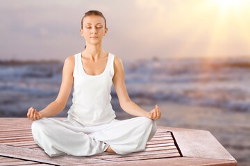 Relaxed young woman practices yoga on sea background