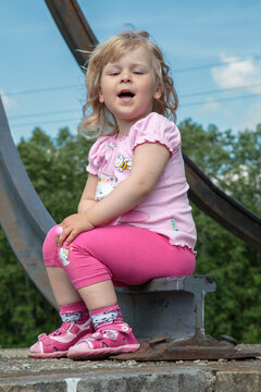 A little girl sits on an old railroad track on a warm summer morning