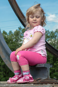 A little girl sits on an old railroad track on a warm summer morning