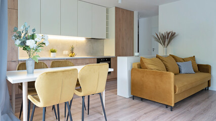 Living room interior with modern yellow sofa, dining room with stylish chairs and kitchen furniture. New design in room in apartment with wooden floor. Banner.	