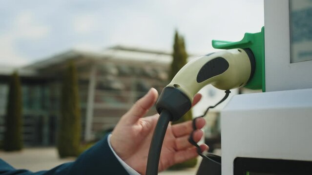 Hand pulling in cable from EV car charger or electric vehicle station. Cable connected at gas station, power supply battery charging an alternative eco environment future technology energy innovation.