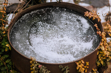 Frozen water, ice with snow in a rusty steel barrel in the garden close-up.