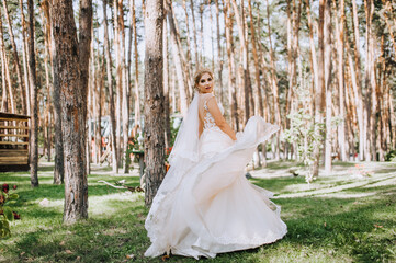 Beautiful, happy, smiling blonde model bride in a long white lace dress dances, spins in a pine face outdoors in nature. Wedding photography, portrait.