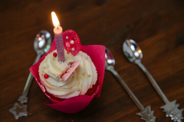 Tasty cupcake for birthday party with candel and spoons on a brown wooden table. Cakes decorated with white cheese cream, pink lollipop and chocolate. For a girls party.