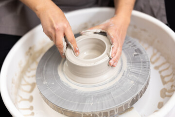 Female potter works with potter weel, craftsman hands close up. Hands of potter making clay pot