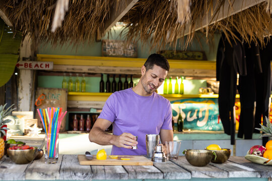 Happy biracial barman preparing cocktail at beach