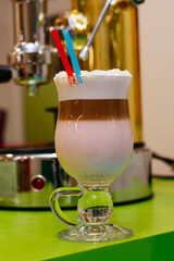 Coffee cocktail with foam and coconut flakes with two straws. Coffee machine on background.