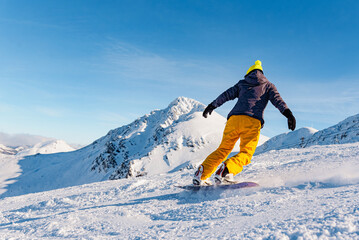unrecognizable person in yellow clothes practicing snowboarding on a ski slope on a sunny day....