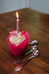 Tasty cupcake for birthday party with candel and spoons on a brown wooden table. Cakes decorated with white cheese cream, pink lollipop and chocolate. For a girls party.