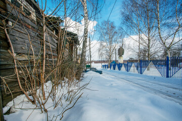 A house with a collapsed roof and walls next to the monument.  about the epic hero Ilya Muromets in Muromek as a symbol of what is happening in Russia: poverty next to a pompous war