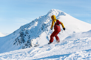 Unrecognizable person descending a ski slope on a snowboard with an impressive snowy mountain in...